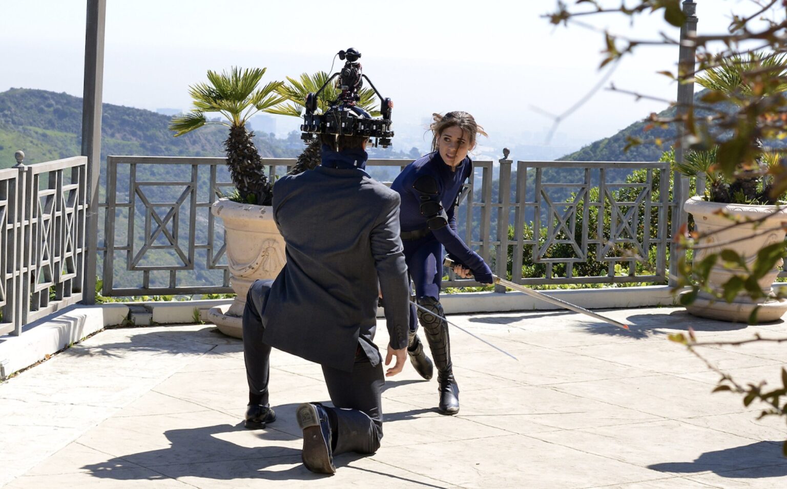 Behind the scenes: a camera operator films a performer with a sword on an outdoor terrace