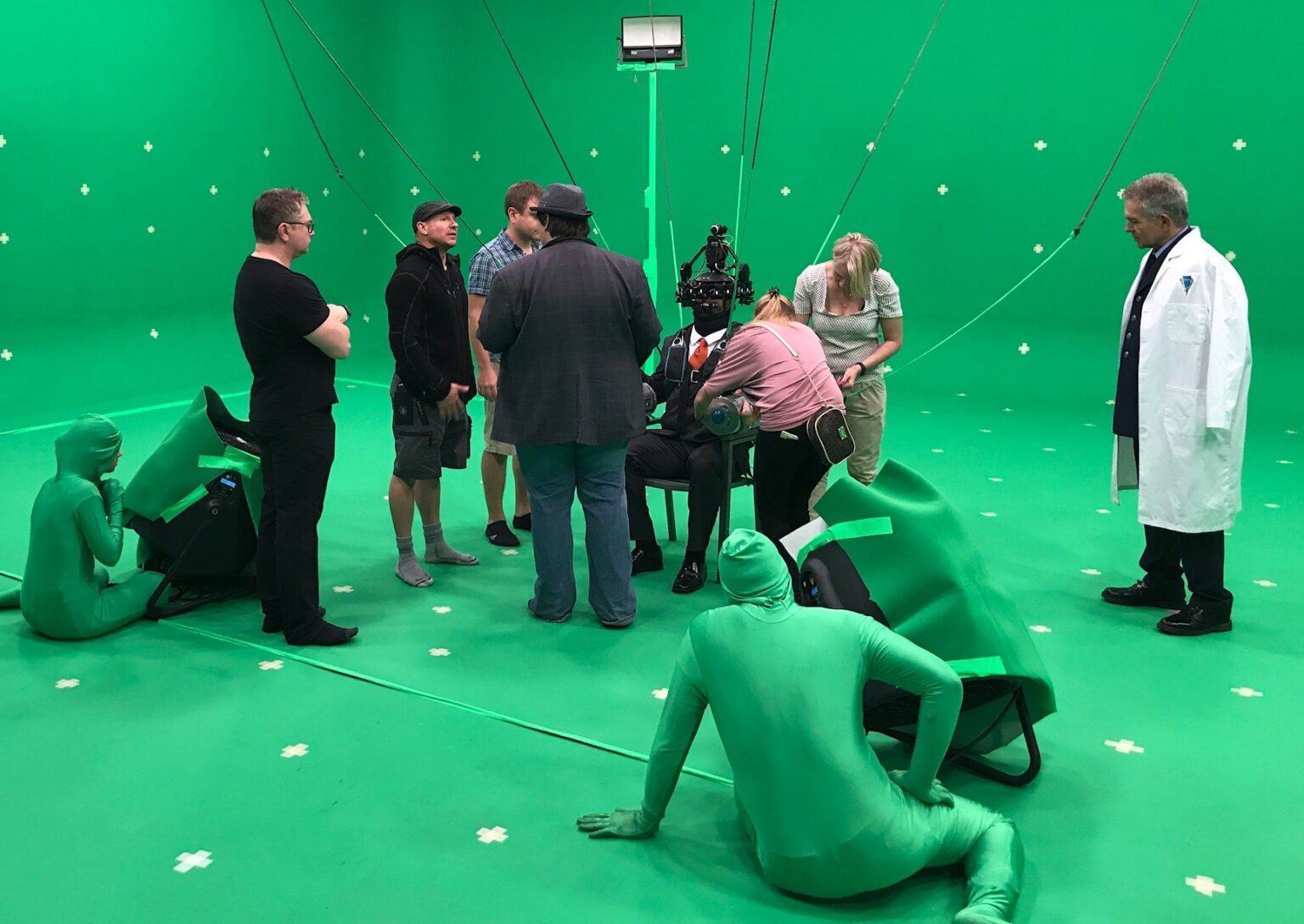 Behind the scenes: cast and crew on a green screen stage, performers in green suits